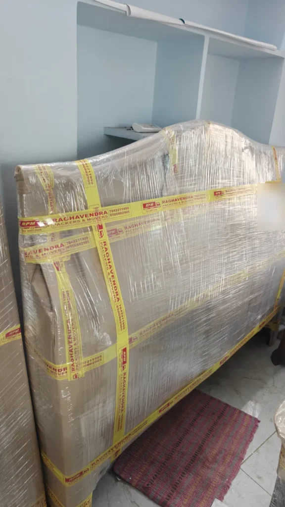 Bed headboard wrapped in stretch film and sealed with Raghavendra Packers and Movers tape in Kakinada